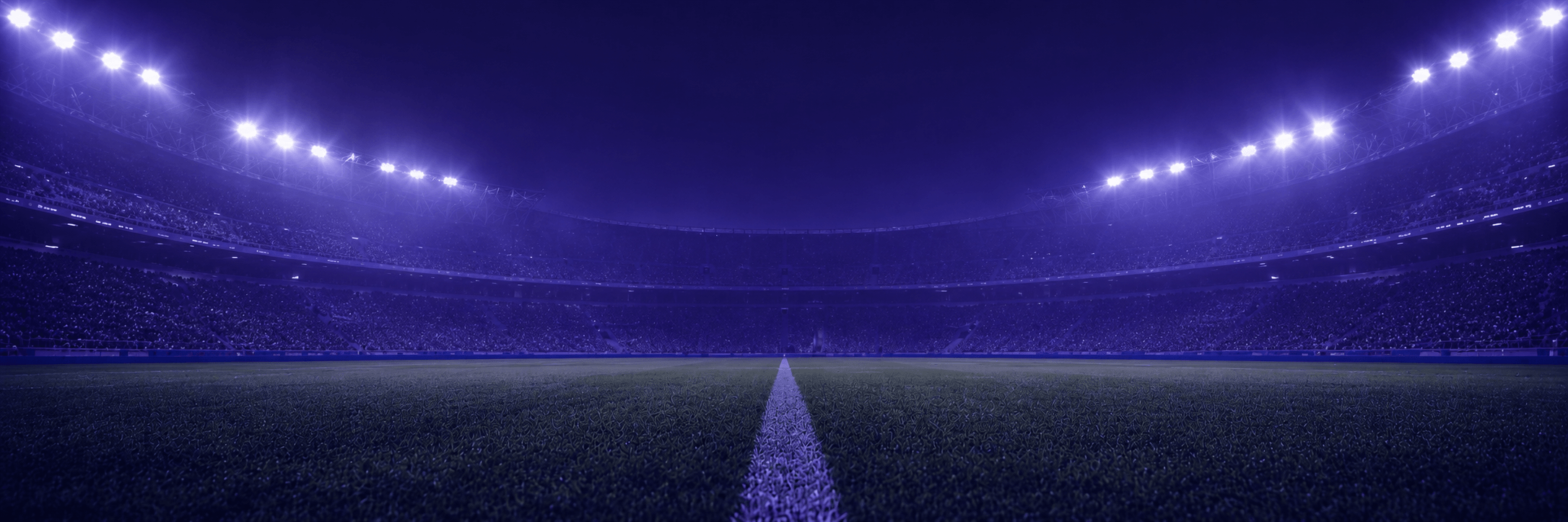 Estadio de fútbol iluminado de noche en tono violeta.
