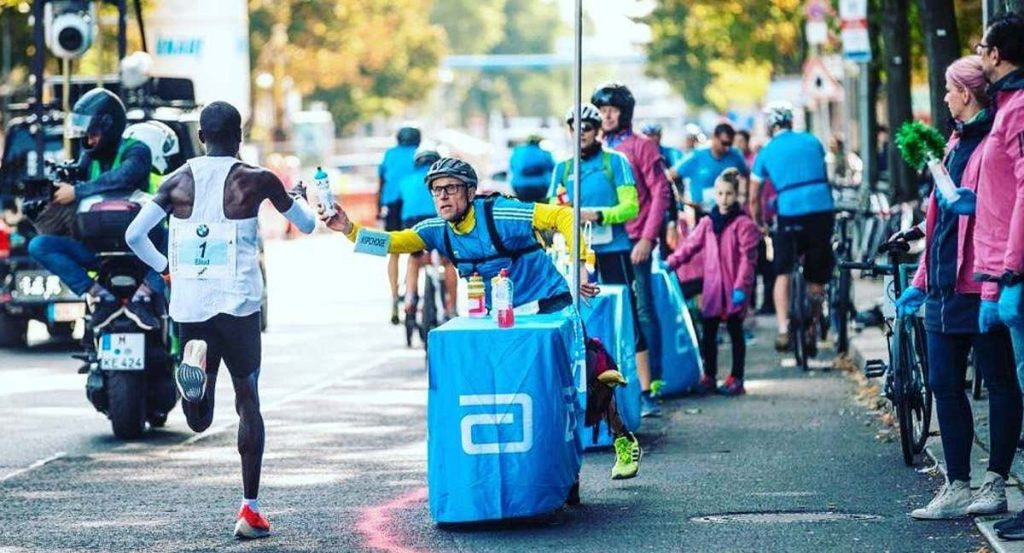 Claus-Henning Schulke entrega un bidón a Kipchoge en la maratón de Berlín de 2018.