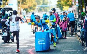 Claus-Henning Schulke entrega un bidón a Kipchoge en la maratón de Berlín de 2018.