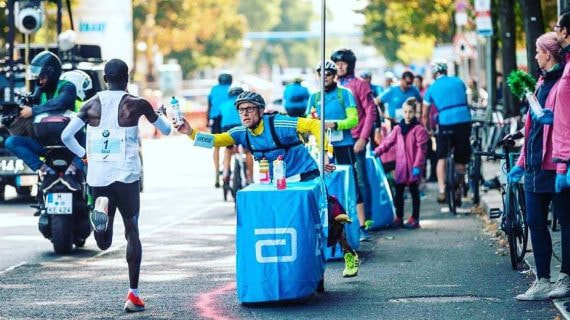 Claus-Henning Schulke entrega un bidón a Kipchoge en la maratón de Berlín de 2018.