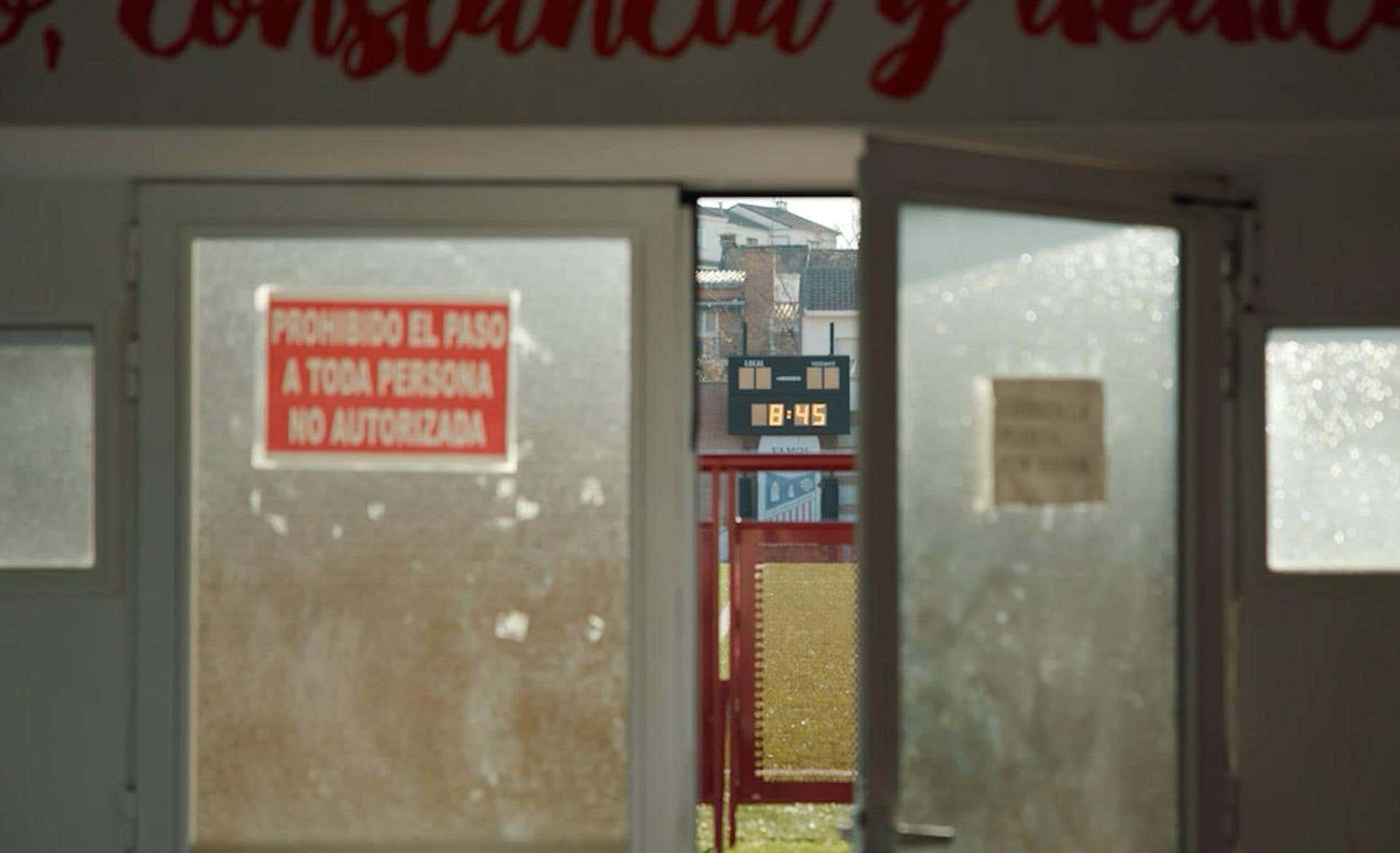 Vista del marcador del estadio del Navalcarnero a través de unas puertas de cristal con un cartel de prohibido el paso
