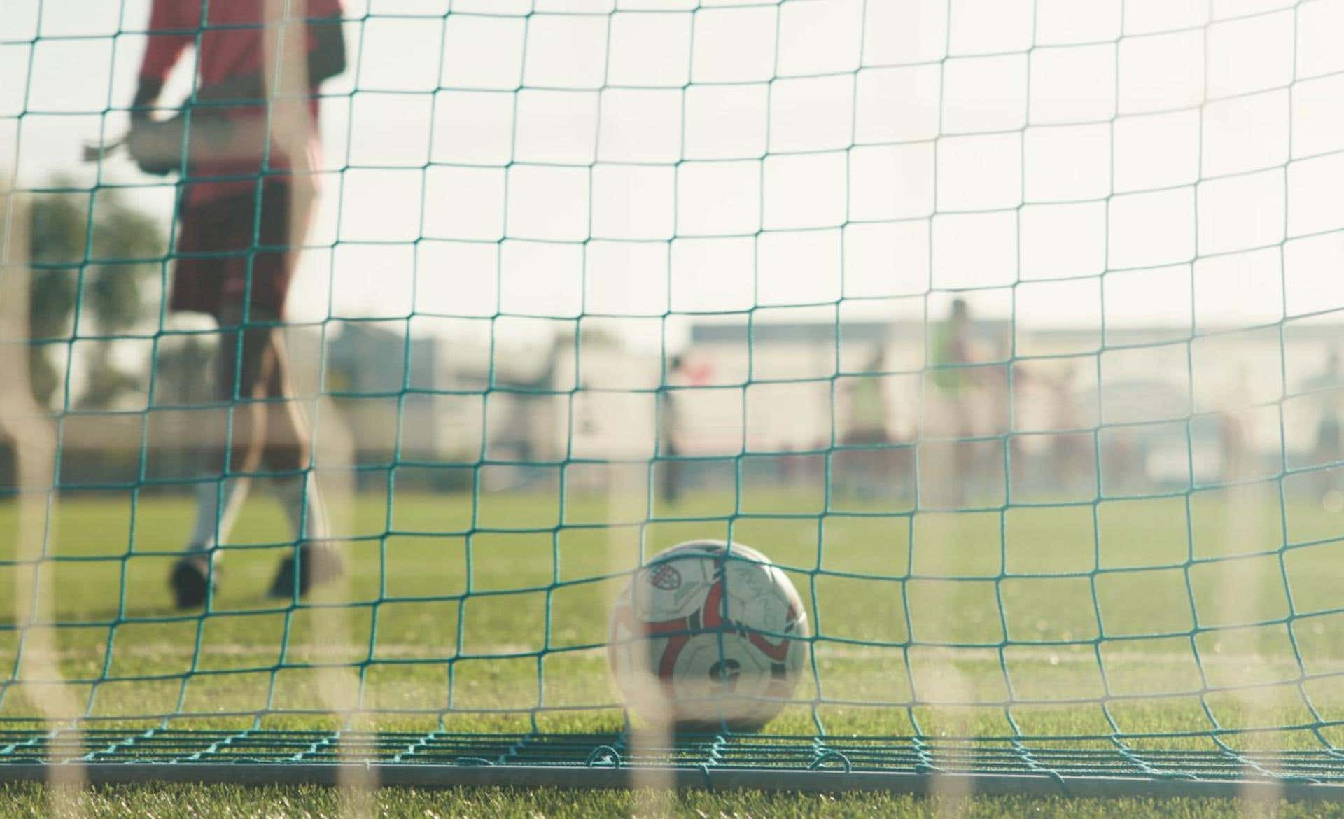 Un balón junto a la red de una portería en un campo de entrenamiento