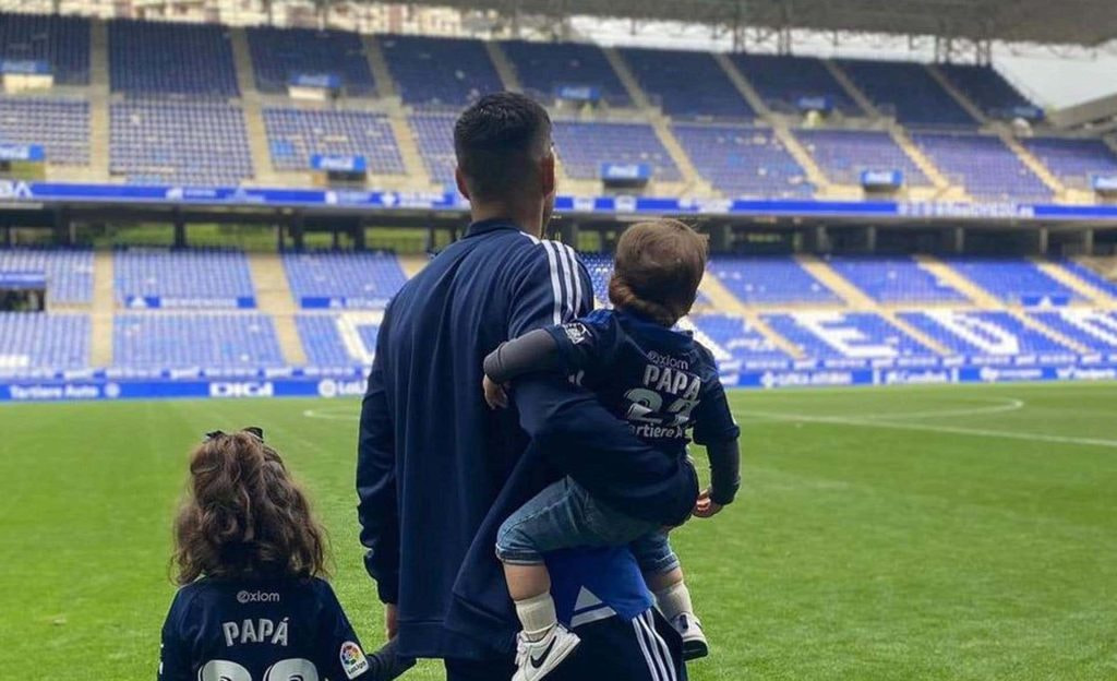 Juanfran, de espaldas en el césped del Carlos Tartiere, sostiene a sus dos hijos; uno viste una camiseta con el dorsal 'Papá'