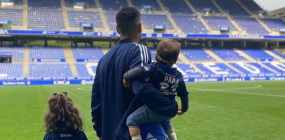 Juanfran, de espaldas en el césped del Carlos Tartiere, sostiene a sus dos hijos; uno viste una camiseta con el dorsal 'Papá'