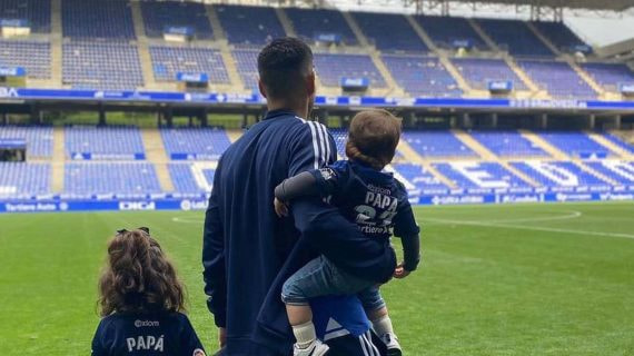 Juanfran, de espaldas en el césped del Carlos Tartiere, sostiene a sus dos hijos; uno viste una camiseta con el dorsal 'Papá'