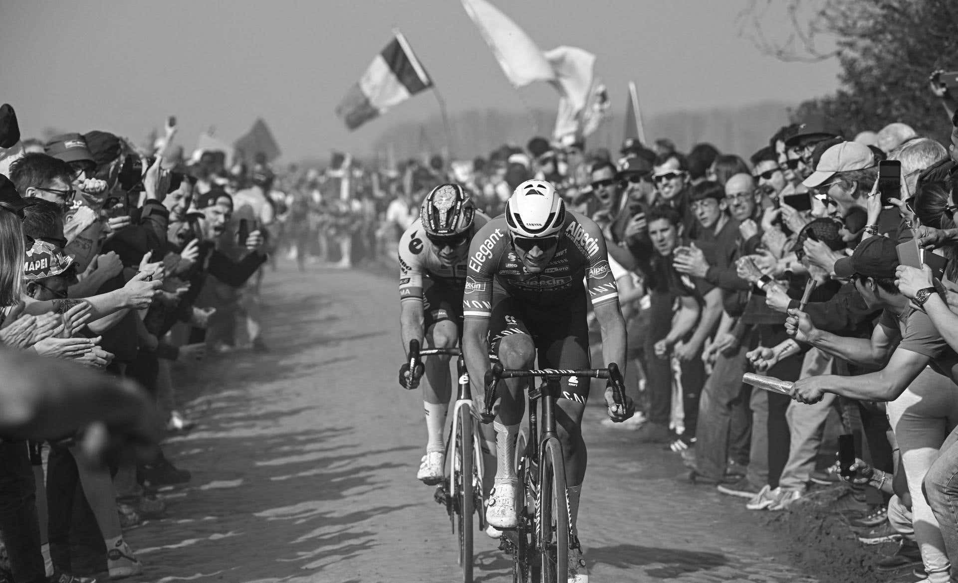 Dos ciclistas ruedan sobre los adoquines entre el público en la París-Roubaix, en blanco y negro