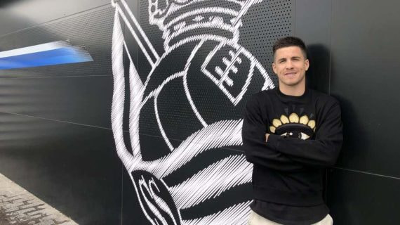 Igor Zubeldia posa con el escudo de la Real Sociedad de fondo.