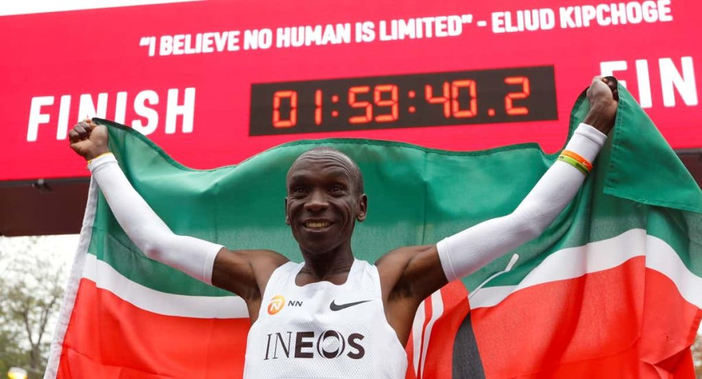 Eliud Kipchoge celebra con la bandera de Kenia bajo el reloj de meta tras bajar de las dos horas en maratón