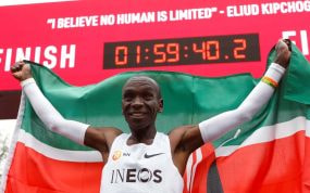 Eliud Kipchoge celebra con la bandera de Kenia bajo el reloj de meta tras bajar de las dos horas en maratón