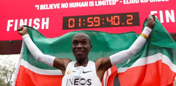 Eliud Kipchoge celebra con la bandera de Kenia bajo el reloj de meta tras bajar de las dos horas en maratón