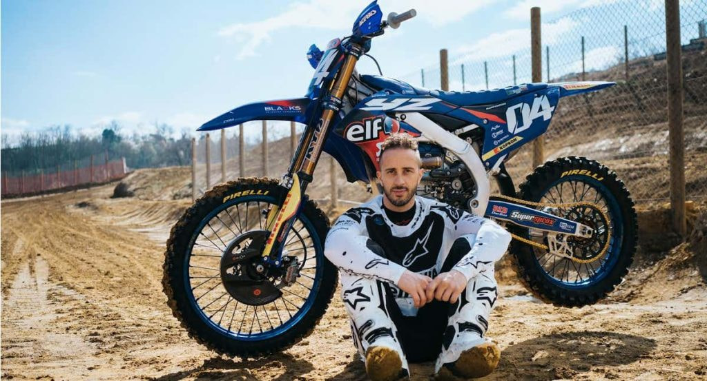 Andrea Dovizioso posa sentado junto a su moto de motocross en un circuito de tierra