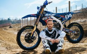 Andrea Dovizioso posa sentado junto a su moto de motocross en un circuito de tierra