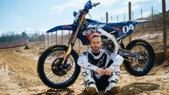 Andrea Dovizioso posa sentado junto a su moto de motocross en un circuito de tierra