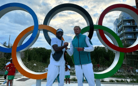 Dos deportistas se estrechan la mano ante los anillos olímpicos de la Villa de los Juegos de París 2024