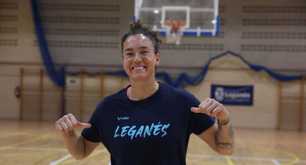 Laura Nicholls sonríe señalando la camiseta del Baloncesto Leganés en el pabellón