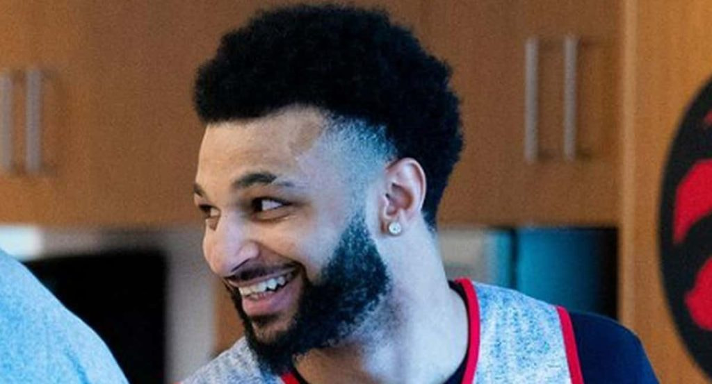 Jamal Murray sonríe en un vestuario con el logo de los Toronto Raptors al fondo