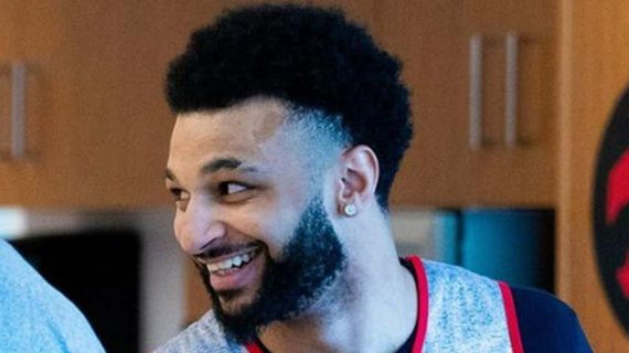 Jamal Murray sonríe en un vestuario con el logo de los Toronto Raptors al fondo
