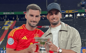 Álex Baena, con la camiseta de España, sostiene el trofeo de la Eurocopa en el estadio Olímpico de Berlín junto a un acompañante
