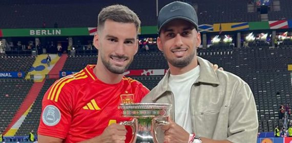 Álex Baena, con la camiseta de España, sostiene el trofeo de la Eurocopa en el estadio Olímpico de Berlín junto a un acompañante