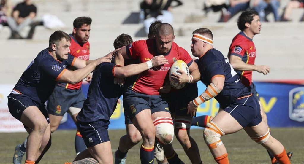 Un delantero de la selección española de rugby avanza con el balón intentando romper varios placajes