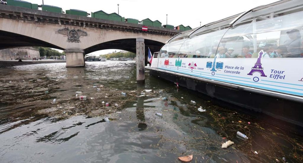 Restos de basura flotan en el Sena junto a un barco turístico bajo un puente de París