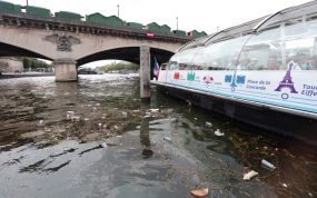 Restos de basura flotan en el Sena junto a un barco turístico bajo un puente de París