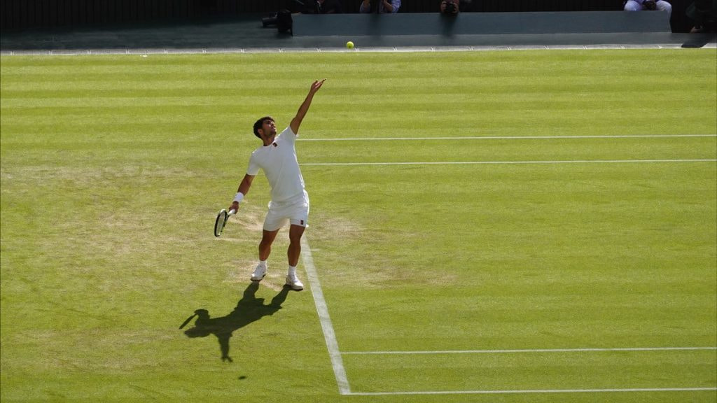 Carlos Alcaraz lanza la bola al aire para sacar sobre la hierba de la pista central de Wimbledon