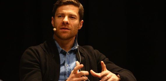 Xabi Alonso gesticula con las manos mientras habla sentado en una charla, con micrófono de diadema y camisa vaquera