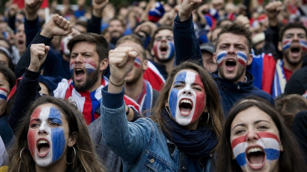 Aficionados con la cara pintada en colores de una selección gritando en una protesta