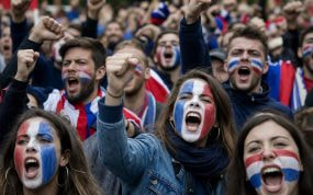 Aficionados con la cara pintada en colores de una selección gritando en una protesta