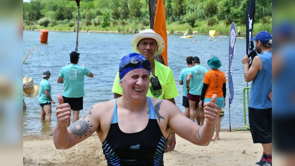 Una nadadora con gorro y gafas levanta los dos pulgares al salir del agua tras una prueba de aguas abiertas