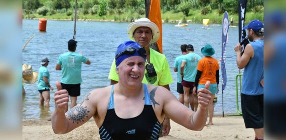 Una nadadora con gorro y gafas levanta los dos pulgares al salir del agua tras una prueba de aguas abiertas