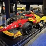 Un monoplaza de IndyCar expuesto en un museo, con coches históricos al fondo