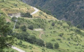 Curvas en zigzag de la subida a Alpe d'Huez entre laderas verdes con el cartel en la ladera, puerto mitico del Tour