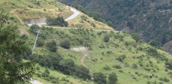 Curvas en zigzag de la subida a Alpe d'Huez entre laderas verdes con el cartel en la ladera, puerto mitico del Tour
