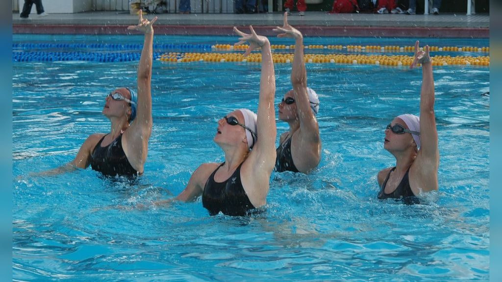 Cuatro nadadoras de natación artística alzan los brazos a la vez en la piscina durante un ejercicio