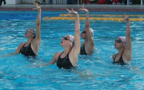 Cuatro nadadoras de natación artística alzan los brazos a la vez en la piscina durante un ejercicio