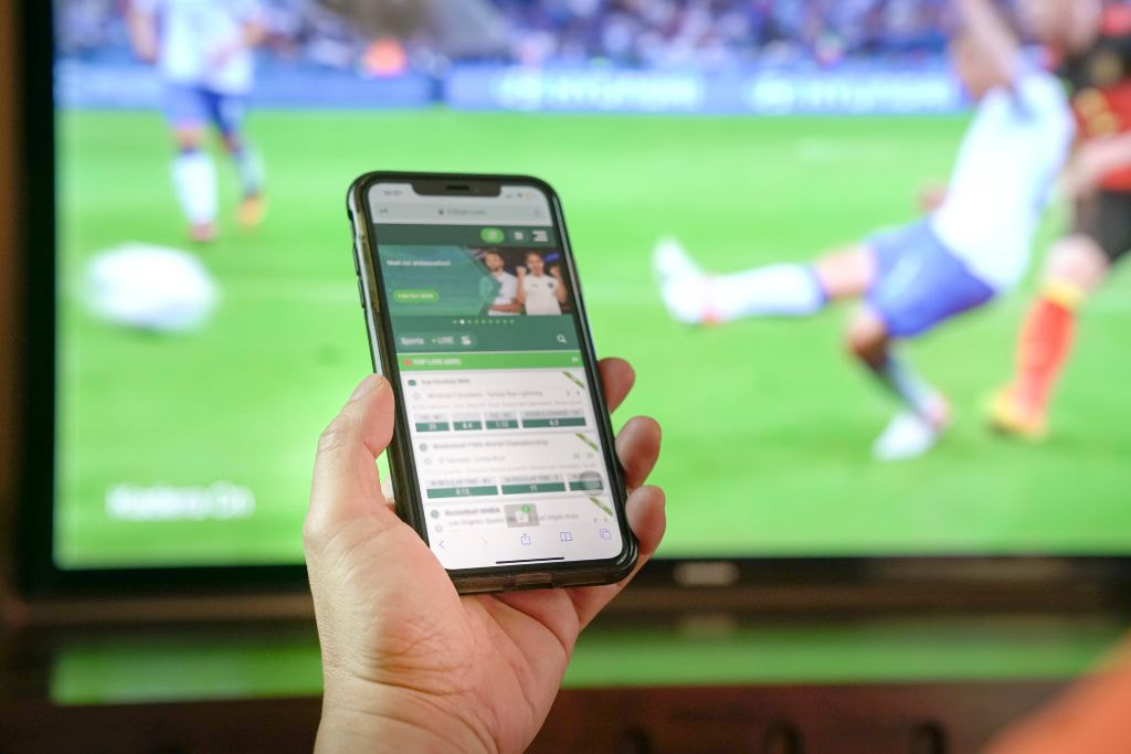 Aficionado siguiendo un partido en directo con la app de apuestas deportivas en la mano