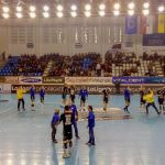 Jugadores de balonmano calientan sobre la pista antes de un partido, con la grada a medio llenar