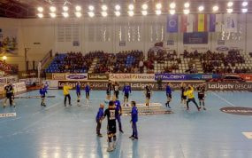 Jugadores de balonmano calientan sobre la pista antes de un partido, con la grada a medio llenar