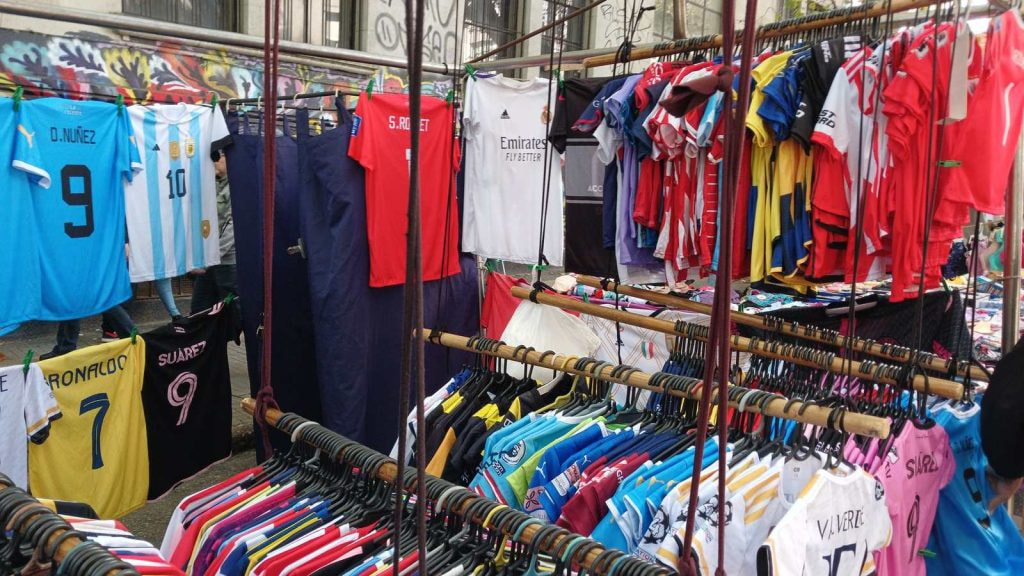 Camisetas de fútbol de selecciones y clubes colgadas a la venta en un puesto de mercado callejero
