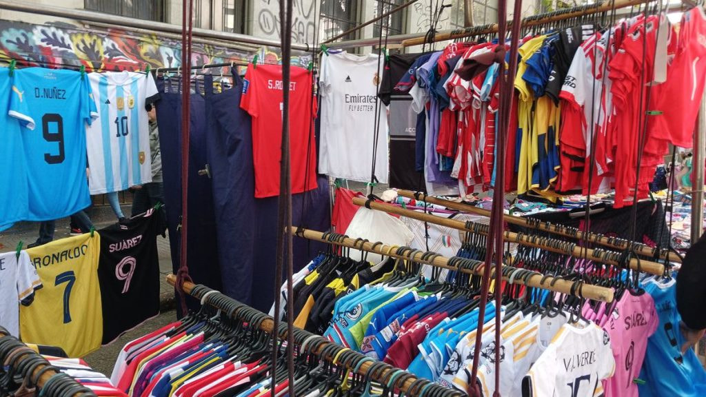 Camisetas de fútbol de varias selecciones y clubes colgadas en un puesto de feria, con una amplia gama de colores