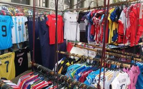 Camisetas de fútbol de varias selecciones y clubes colgadas en un puesto de feria, con una amplia gama de colores