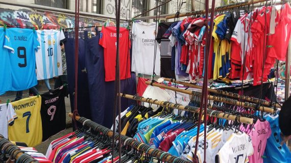 Camisetas de fútbol de varias selecciones y clubes colgadas en un puesto de feria, con una amplia gama de colores
