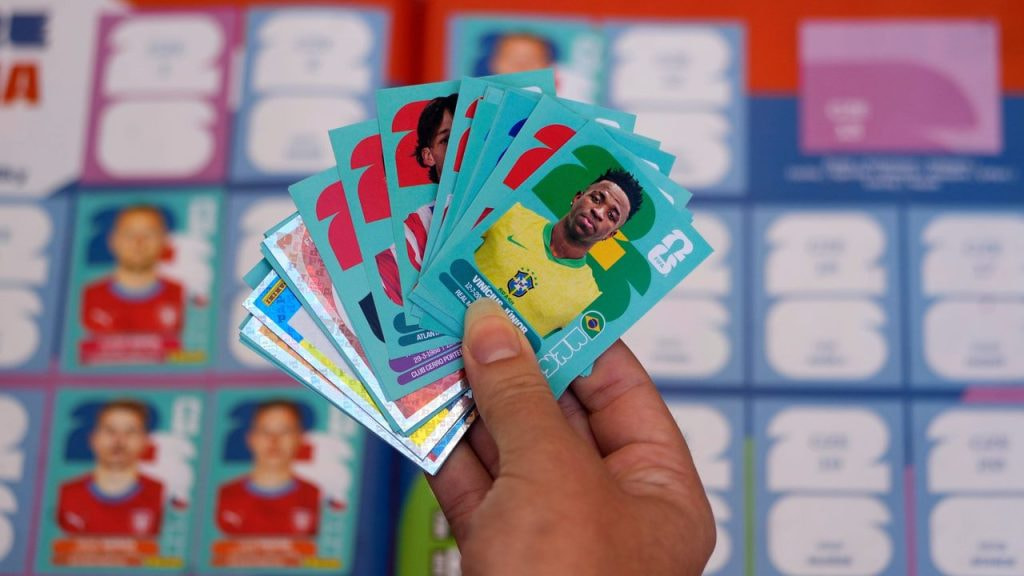 Un aficionado con varios cromos del Mundial 2026 en la mano, entre ellos el de Vinícius Jr. con Brasil.