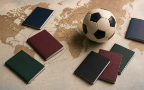 Pasaportes de distintos colores y un balón de fútbol sobre un mapamundi con rutas migratorias entre continentes