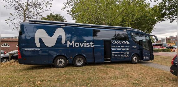 El autobús del equipo ciclista Movistar aparcado bajo unos árboles antes de una etapa