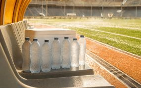 Botellas de agua heladas junto a una nevera en un banquillo vacío bajo el calor de un estadio de fútbol