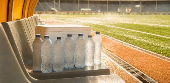 Botellas de agua heladas junto a una nevera en un banquillo vacío bajo el calor de un estadio de fútbol