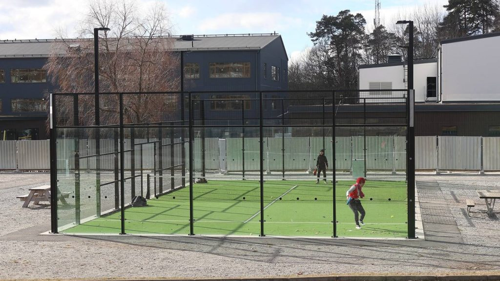 Partido de padel en una pista exterior con paredes de cristal y cesped verde, dos jugadores en plena accion de juego